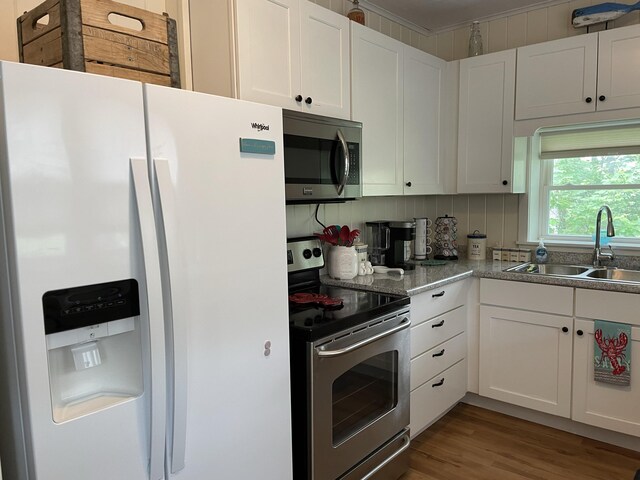 kitchen featuring a sink, backsplash, wood finished floors, stainless steel appliances, and white cabinets