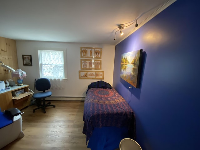 bedroom with rail lighting, wood finished floors, baseboard heating, and ornamental molding