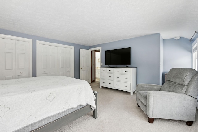 bedroom featuring light carpet, vaulted ceiling, a textured ceiling, and two closets