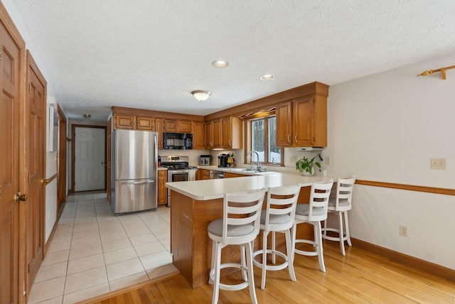 kitchen featuring appliances with stainless steel finishes, a breakfast bar, brown cabinets, a peninsula, and light countertops