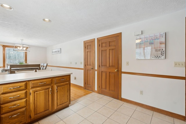 kitchen with brown cabinetry, light countertops, a textured ceiling, and light tile patterned floors