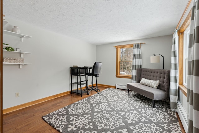 living area featuring a textured ceiling, baseboard heating, wood finished floors, and baseboards