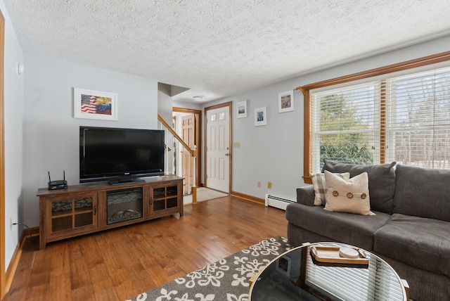 living area featuring a baseboard heating unit, a textured ceiling, wood finished floors, and baseboards