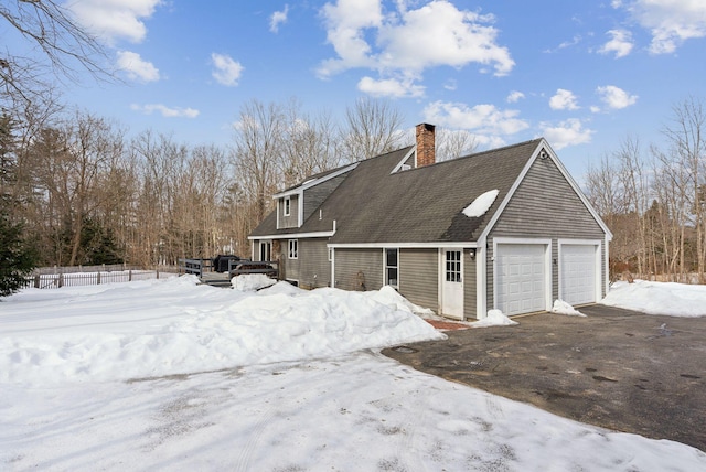 view of snowy exterior featuring a detached garage, a chimney, and roof with shingles