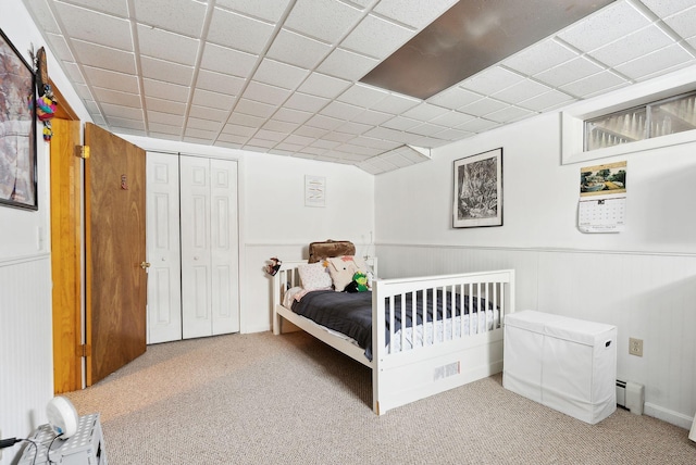 carpeted bedroom featuring a paneled ceiling, a baseboard heating unit, and wainscoting