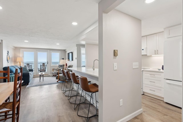 191 E Grand Ave Unit 606, Old Orchard Beach, ME 04064 - kitchen with freestanding refrigerator, a breakfast bar area, light wood finished floors, open floor plan, and white cabinetry
