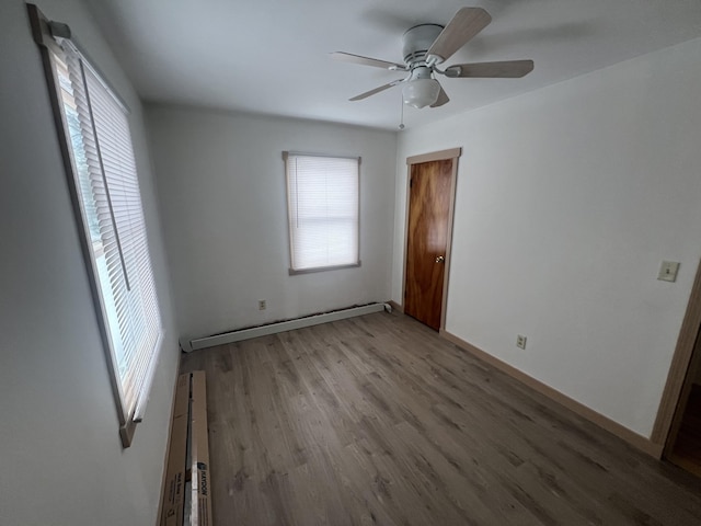 unfurnished bedroom with a ceiling fan, multiple windows, a baseboard heating unit, and wood finished floors