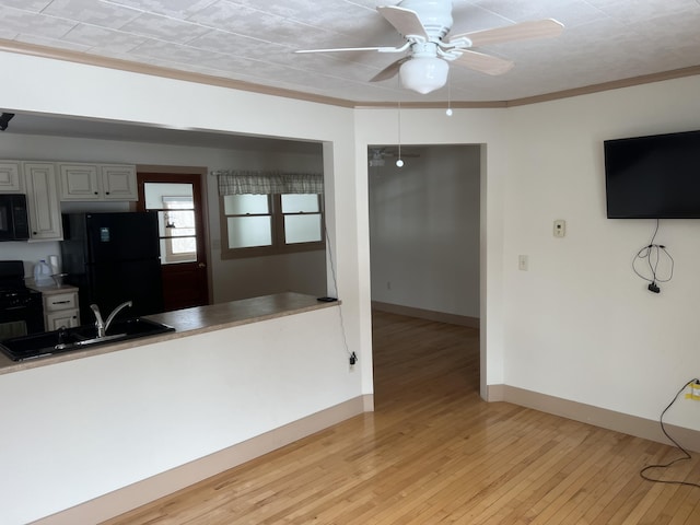 kitchen with light wood-style floors, a ceiling fan, a sink, black appliances, and baseboards