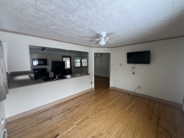 unfurnished living room featuring baseboards, ceiling fan, ornamental molding, light wood-type flooring, and a sink