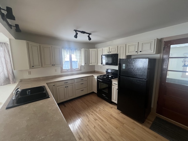 kitchen featuring light wood finished floors, rail lighting, light countertops, black appliances, and a sink