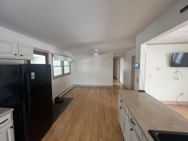 kitchen featuring light wood finished floors, white cabinetry, a baseboard heating unit, and freestanding refrigerator