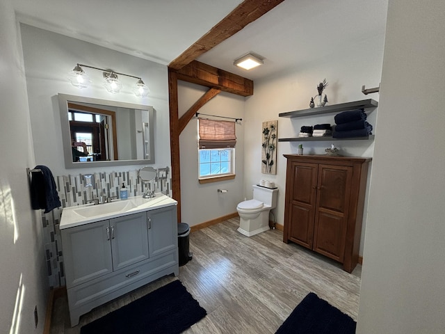 half bath featuring tasteful backsplash, baseboards, toilet, wood finished floors, and vanity