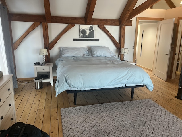 bedroom featuring light wood-style flooring, baseboards, and beamed ceiling