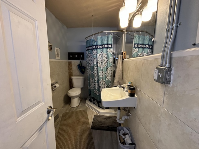 bathroom with tile walls, wainscoting, toilet, a shower with curtain, and a sink