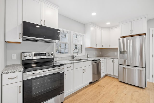 kitchen with light stone counters, light wood-style flooring, a sink, white cabinets, and appliances with stainless steel finishes