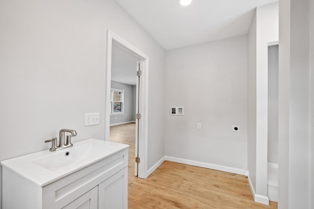 laundry room featuring baseboards, hookup for an electric dryer, light wood-type flooring, washer hookup, and a sink