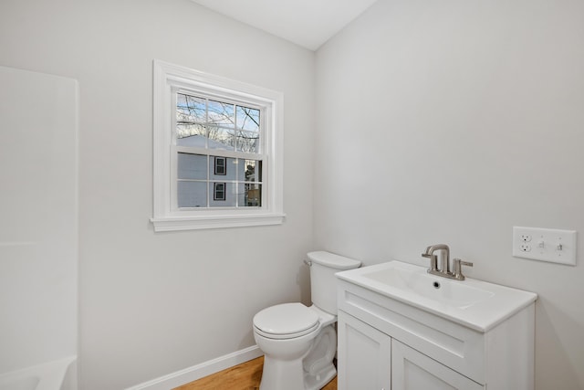 bathroom featuring baseboards, toilet, wood finished floors, a bathtub, and vanity