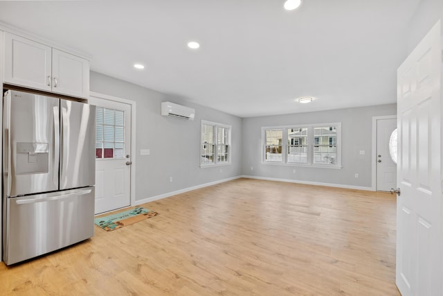 kitchen featuring light wood finished floors, baseboards, white cabinets, stainless steel fridge with ice dispenser, and a wall mounted AC