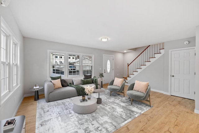 living area with light wood-style floors, baseboards, and stairway