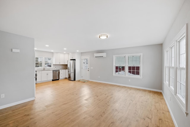 unfurnished living room featuring light wood-style flooring, recessed lighting, a sink, baseboards, and a wall mounted AC