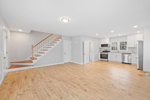 unfurnished living room with recessed lighting, a sink, baseboards, stairs, and light wood-style floors