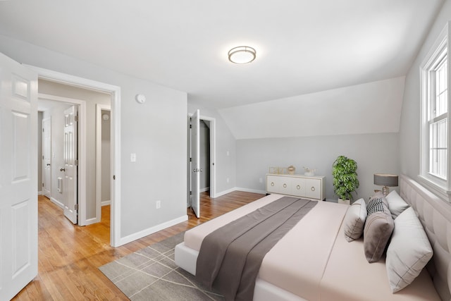 bedroom with light wood-style floors, baseboards, and vaulted ceiling