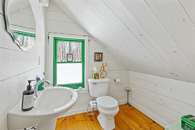 bathroom featuring wooden walls, toilet, lofted ceiling, wood finished floors, and a sink