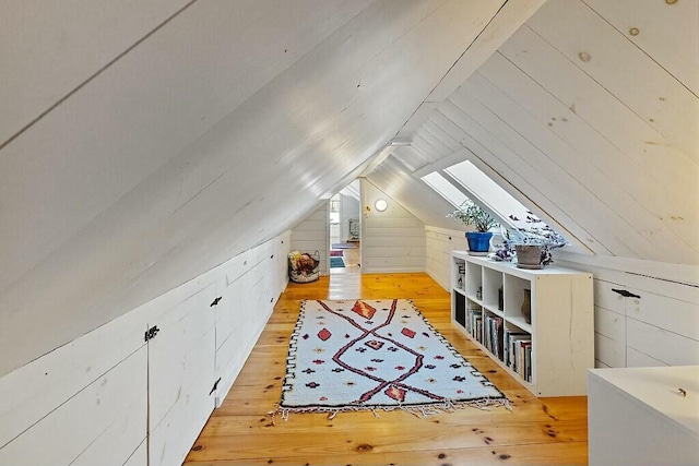 additional living space featuring light wood-style floors, lofted ceiling with skylight, and wood walls