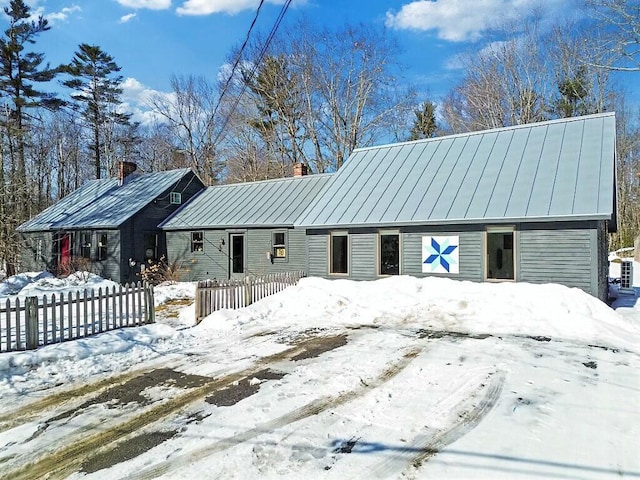 view of front of house featuring a standing seam roof, metal roof, a chimney, and fence