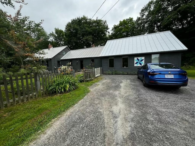 view of front of property with metal roof, a standing seam roof, gravel driveway, and fence