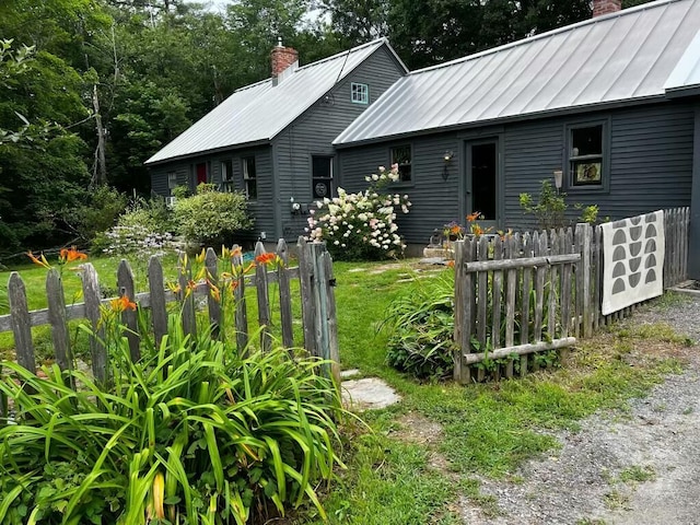 view of front facade featuring a standing seam roof, a chimney, fence, and metal roof