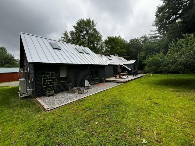 rear view of house featuring a standing seam roof, metal roof, a deck, and a yard