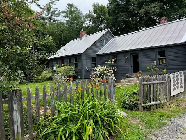 view of front facade with a standing seam roof, metal roof, a chimney, and fence