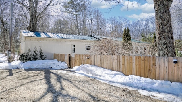 view of snowy exterior featuring metal roof and fence