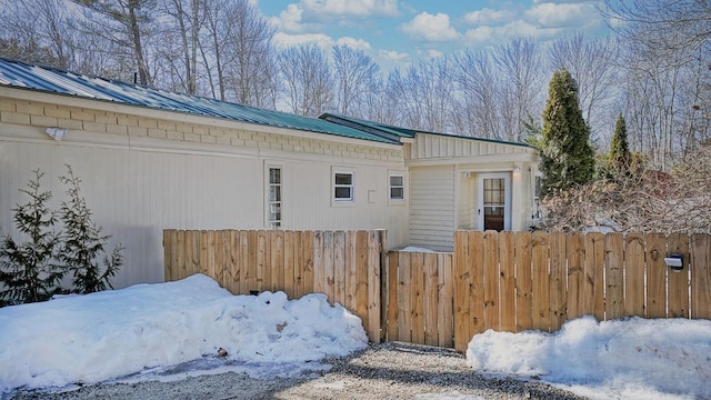 view of snowy exterior with metal roof and fence