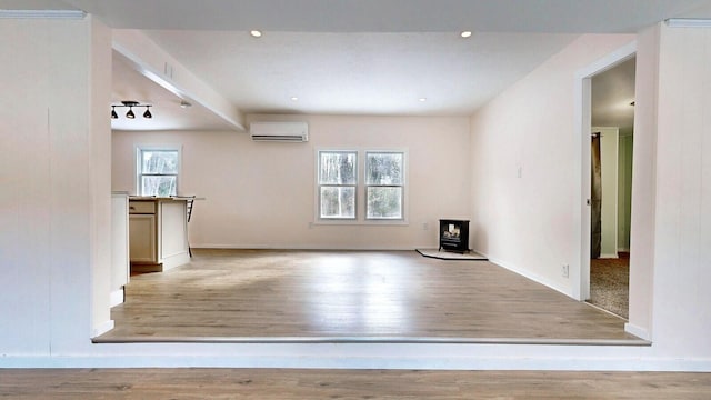 unfurnished living room with a wood stove, wood finished floors, a wealth of natural light, and a wall mounted AC