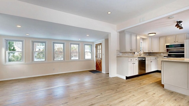 kitchen with backsplash, open floor plan, light countertops, appliances with stainless steel finishes, and light wood-style floors