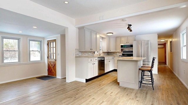 kitchen with a kitchen bar, light wood-style flooring, tasteful backsplash, appliances with stainless steel finishes, and light countertops