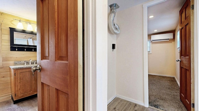 bathroom with wood finished floors, a wall unit AC, wooden walls, baseboards, and vanity