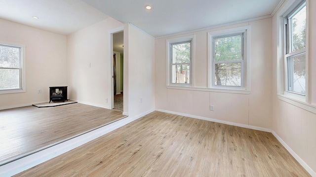 unfurnished room featuring a wood stove, recessed lighting, baseboards, and light wood-type flooring