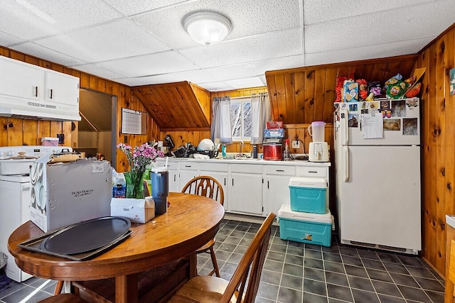 kitchen featuring dark tile patterned flooring, freestanding refrigerator, wood walls, under cabinet range hood, and white cabinetry