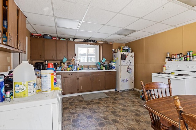 kitchen with white appliances, brown cabinetry, light countertops, a paneled ceiling, and a sink