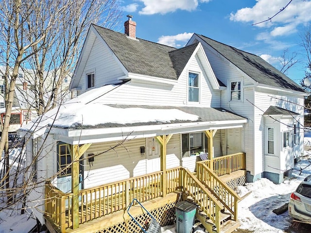 snow covered back of property with a porch, roof with shingles, and a chimney