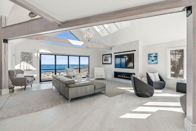 living room featuring a healthy amount of sunlight, a skylight, beam ceiling, and a glass covered fireplace