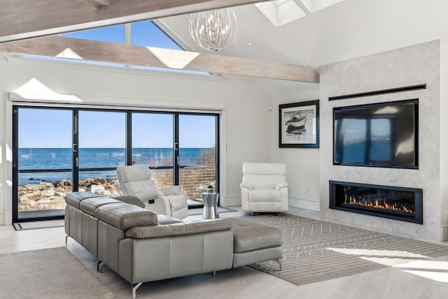 living room with a large fireplace, vaulted ceiling with skylight, baseboards, light wood-style flooring, and an inviting chandelier