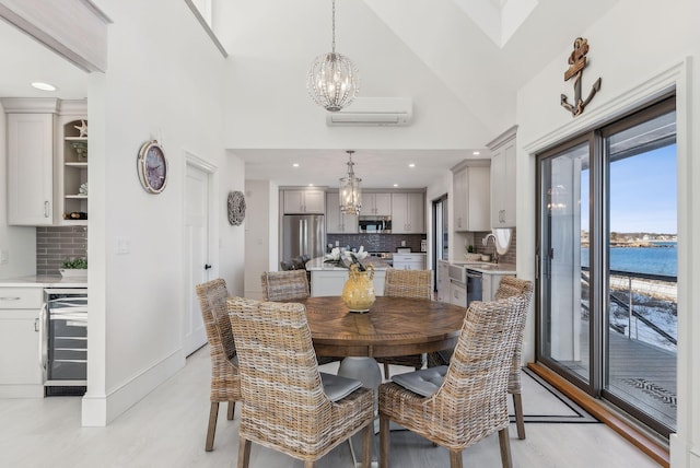 dining area with high vaulted ceiling, a water view, an AC wall unit, a chandelier, and beverage cooler