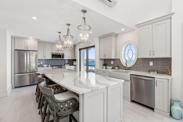 kitchen featuring a kitchen island, appliances with stainless steel finishes, light stone countertops, a kitchen bar, and a sink