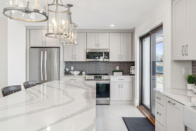 kitchen featuring pendant lighting, appliances with stainless steel finishes, light stone counters, and decorative backsplash