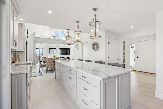 kitchen with open floor plan, a sink, light wood-style flooring, and light stone countertops