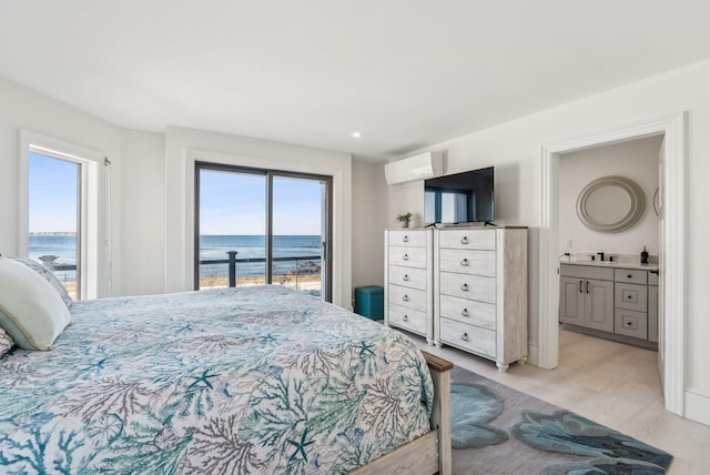 bedroom with light wood-type flooring, access to outside, a wall mounted air conditioner, and ensuite bath